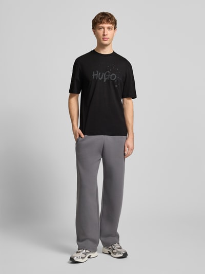 Männermodel trägt Regular Fit T-Shirt aus reiner Baumwolle Modell 'NIEROFIX_U261' von HUGO, Optik: Unifarben, Motiv-Print, Rundhals, Kurzarm, Label-Stitching-Applikation, Ganzkörperansicht von vorne.