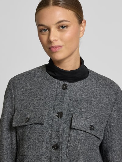 Kobiece modelka nosi Taillierter Kurzblazer aus Viskose-Woll-Mix od Marc O'Polo, efekt: jednolity kolor, taliowany krój, okrągły dekolt, listwa guzikowa, długi rękaw, rozcięcie z zapięciem na guzik, kieszeń na piersi, materiał: mieszanka wiskozy i wełny, kolor szary, tekstura miękka, widok: zbliżenie na górę ciała.