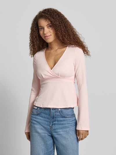 Frauenmodel trägt Regular Fit Langarmshirt in Wickel-Optik Modell 'PELLY' von Only, Struktur-Muster, Trompetenärmel, tiefer V-Ausschnitt, Bindeband, Farbe zartrosa, Ganzkörperansicht von vorne.