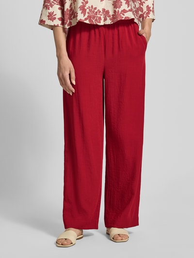 Frauenmodel trägt spodnie materiałowe z mieszanki wiskozy z tunelem Modell 'Daria' von MSCH Copenhagen, krój relaxed fit, szerokość w rozmiarze S: 39 cm, długość wewnętrzna nogawki w rozmiarze S: 78 cm, czerwona faktura, zbliżenie na dolną część ciała, widok z przodu.