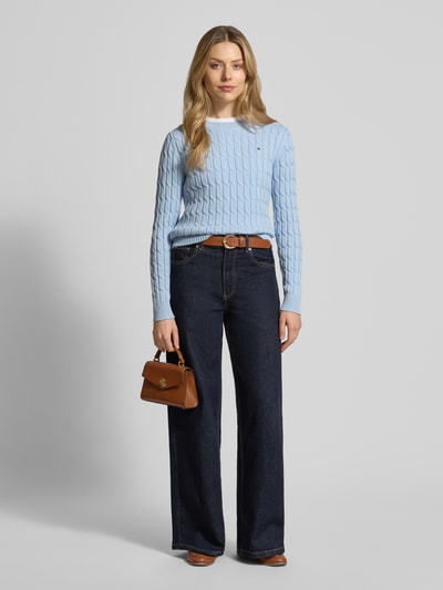 Modelka nosi Slim Fit Strickpullover aus reiner Baumwolle od Tommy Hilfiger, jasnoniebieski, prążkowany, logo, okrągły dekolt, krój slim fit, bawełna, widok całej sylwetki z przodu.