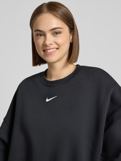 Frauenmodel trägt Sweatshirt mit Logo Modell 'Phoenix' von Nike aus Baumwoll-Elasthan-Mix in Schwarz, Nahaufnahme Oberkörper.