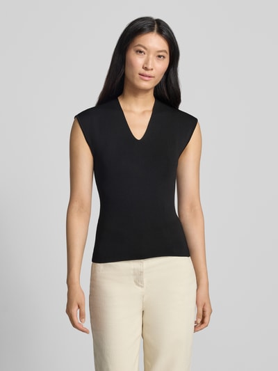 Frauenmodel trägt Stricktop mit V-Ausschnitt Modell 'CANELONS' von MANGO, taillierter Schnitt in Schwarz, feine Textur, Ganzkörperansicht von vorne.