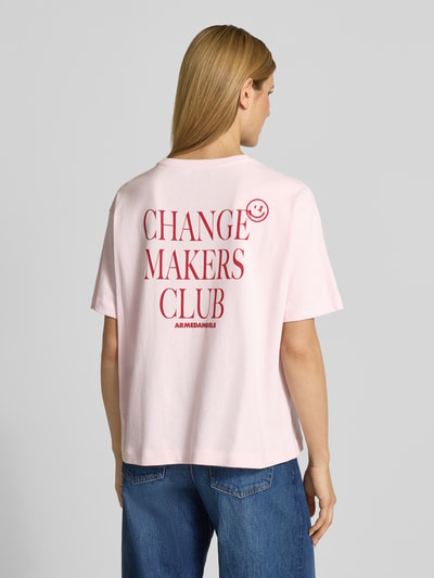 Frauenmodel trägt Oversized T-Shirt aus reiner Baumwolle Modell 'GIANNAA CHAANGE' von Armedangels in Rosa mit Label Print, unifarben, Feinrippstruktur, Ganzkörperansicht Rückansicht.