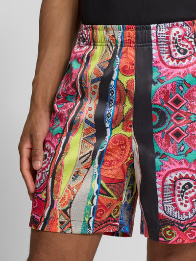 Männermodel trägt bunte Straight Fit Shorts mit elastischem Bund Modell 'Resort' von COLUCCI, Mix aus leuchtenden Farben und Mustern, Nahaufnahme Oberkörper, Kontext: elastischer Material-Mix, Herrenshorts, Bundweite 39 cm, Innenbeinlänge 16 cm bei Größe M.