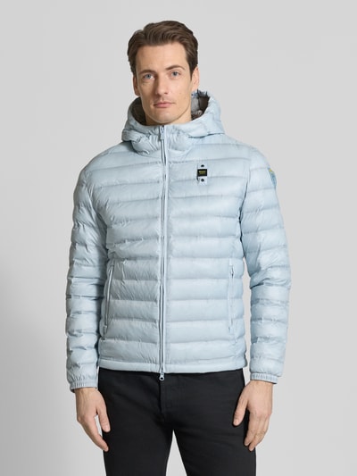 Männermodel trägt hellblaue Steppjacke mit Zweiwege-Reißverschluss Modell 'Charles' von Blauer Usa, Regular Fit, Kapuze, Ganzkörperansicht von vorne, Label-Detail, Rückenlänge Größe M 65 cm, Schulterbreite 47 cm, Brustweite 55 cm, Ärmellänge 65 cm.