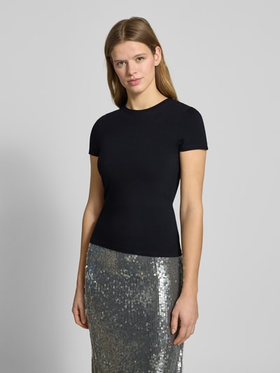 Modelka nosi Slim Fit T-Shirt mit Rundhalsausschnitt od REVIEW, damski t-shirt, elastyczna mieszanka bawełny, krój slim fit, okrągły dekolt, krótki rękaw, długość tyłu w rozmiarze S: 52 cm, czarny kolor, gładka faktura, pełny widok z przodu.