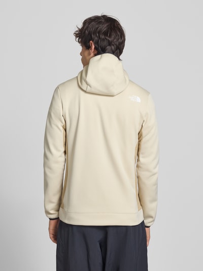 Männermodel trägt Funktionsjacke mit Napoleontasche Modell 'MOUNTAIN ATHLETICS' von The North Face in Beige, Slim-Fit, Kapuze, Ganzkörperansicht Rückansicht. Rückenlänge 70 cm, Ärmellänge 68 cm bei Größe M, elastische Ärmelabschlüsse, Eingrifftaschen.