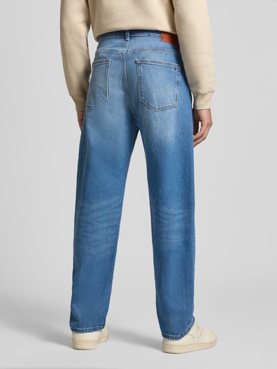 Männermodel trägt Tapered Fit Jeans aus Baumwoll-Mix von Tommy Jeans in mittelblauem Denim mit Label Patch, 5-Pocket-Design, Ganzkörperansicht Rückansicht.