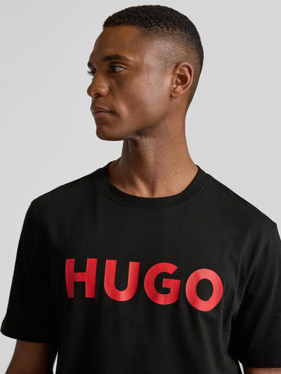 Mannelijk model draagt T-shirt met Label-Schriftzug Modell 'DULIVIO' van HUGO, zwart, katoen, rood logo, rechte pasvorm, Nahaufnahme bovenlichaam.