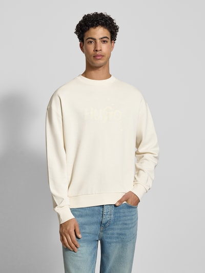 Männermodel draagt Regular Fit Sweatshirt aus reiner Baumwolle Modell 'NIEROFIX_CREW' van HUGO, unie crème, label print, crew neck, lange mouwen, gebreide boorden, vooraanzicht bovenlichaam.