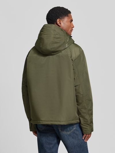 Männermodel trägt Jacke mit Kapuze und kurzem Reißverschluss von Napapijri in Olivgrün, strukturierter Stoff, Ganzkörperansicht Rückansicht, Modell 'RAINFOREST NEXT', gerader Schnitt, Kapuze mit Tunnelzug und Kordelstoppern, Pattentasche, Label-Patches.