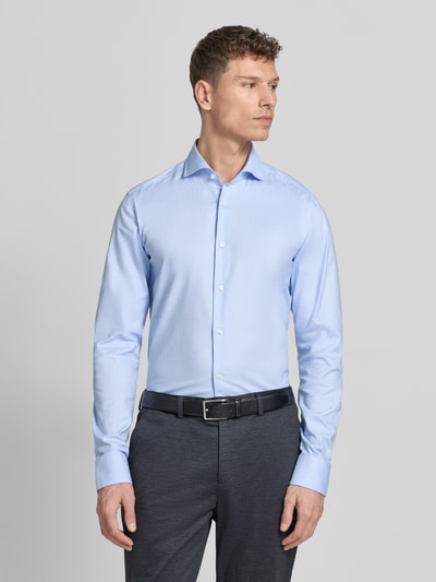 Męski model nosi Regular Fit Businesshemd mit extra langem Arm od BOSS, jasnoniebieska bawełniana koszula, jednolity kolor, krój regular fit, kołnierz typu kent, długi rękaw z mankietami, zaokrąglony dół, materiał bawełniany, zdjęcie całej sylwetki z przodu.