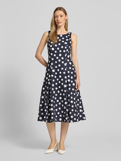 Frauenmodel trägt Cocktailkleid im Allover-Look von Vera Mont in Dunkelblau mit weißen Punkten, A-Linie, Material-Mix mit Stretch-Anteil, Midikleid, Rundhalsausschnitt, Ganzkörperansicht von vorne. Rückenlänge bei Größe 36: 32 cm, Brustweite bei Größe 36: 36 cm.