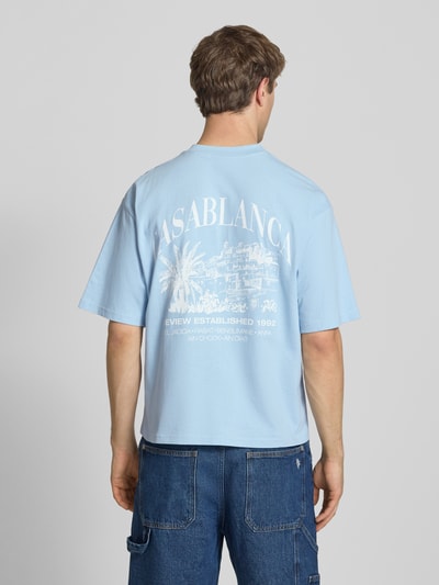 Männermodel trägt T-Shirt mit Label-Detail von REVIEW in Hellblau, Reine Baumwolle, Lockerer-Schnitt, Rundhalsausschnitt, 1/2-Arm, Rückenlänge 68 cm, Ganzkörperansicht Rückansicht.