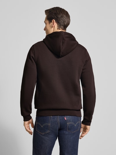 Mężczyzna nosi Regular Fit Sweatjacke aus Baumwoll-Mix od Lacoste, jednokolorowa, dzianina dresowa, kaptur, aplikacja z logo, krój regular fit, zamek błyskawiczny, prążkowane wykończenia, przednie kieszenie, mieszanka bawełny, widok całej sylwetki od tyłu.