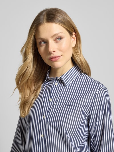 Frauenmodel trägt Regular Fit Bluse mit Streifenmuster und Label-Stitching von Gant in Blau-Weiß aus reiner Baumwolle, Nahaufnahme Oberkörper.