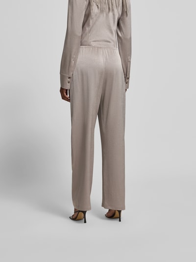 Vrouwenmodel draagt Stoffhose met elastische band van Nanushka in taupe fluweel, relaxed fit, siernaden, volledig zicht van achteren.