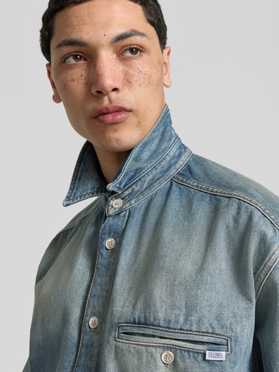 Männermodel trägt Relaxed Fit Jeanshemd aus Reine Baumwolle von MM6 Maison Margiela im Used-Look mit Durchgehender Knopfleiste, Nahaufnahme Oberkörper.