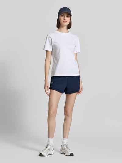 Frauenmodel trägt Regular Fit Sweatshorts mit Logo-Applikation von Lacoste, Optik: Unifarben, Passform: Regular-Fit, Materialverarbeitung: Sweat, mit seitlichen Eingrifftaschen und elastischem Bundabschluss, Ganzkörperansicht von vorne.