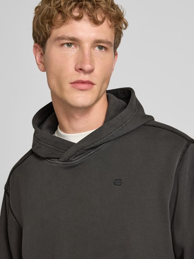 Männermodel trägt Regular Fit Hoodie aus reiner Baumwolle von G-Star RAW in Dunkelgrau, glatte Struktur, Nahaufnahme Oberkörper.