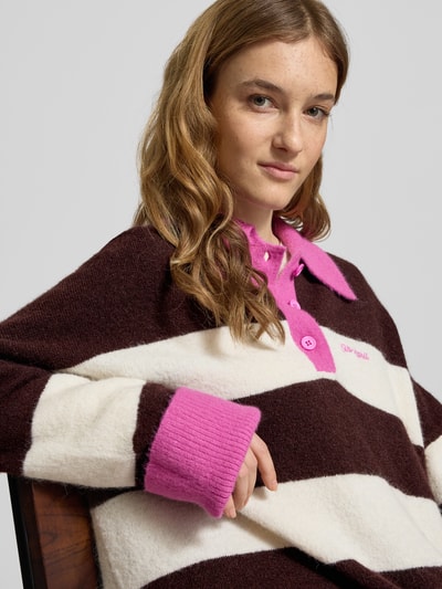 Frauenmodel trägt Oversized Strickpullover mit Polokragen Modell 'Maya' von OH APRIL, braun-weiß gestreift mit pinken Details, Material-Mix, Label-Stitching, Nahaufnahme Oberkörper.