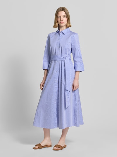 Frauenmodel trägt Midikleid mit Hemdblusenkragen Modell 'Alina' von Christian Berg Woman, blaue Streifen, reine Baumwolle, taillierte Passform, 3/4-Arm, Taillenband, durchgehende Knopfleiste, Ganzkörperansicht von vorne.