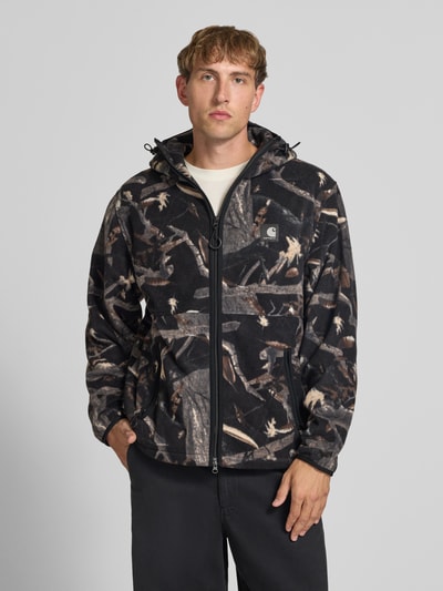 Männermodel trägt Fleecejacke mit Kapuze Modell 'Blevin' von Carhartt Work In Progress in Schwarz mit Naturmuster und Label-Patch, Nahaufnahme Oberkörper, gerader Schnitt, Zwei-Wege-Reißverschluss, Kapuze, Seitentaschen