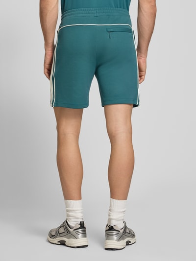 Männermodel trägt Shorts mit Logo-Stitching Modell 'EGEO' von SERGIO TACCHINI in Türkis mit weißen Streifen, lockerer Schnitt, Ganzkörperansicht Rückansicht.