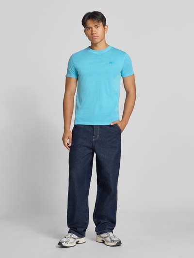 Männermodel trägt T-Shirt mit Rundhalsausschnitt und Label-Stitching von Superdry, Slim Fit, reine Baumwolle, Ganzkörperansicht von vorne.