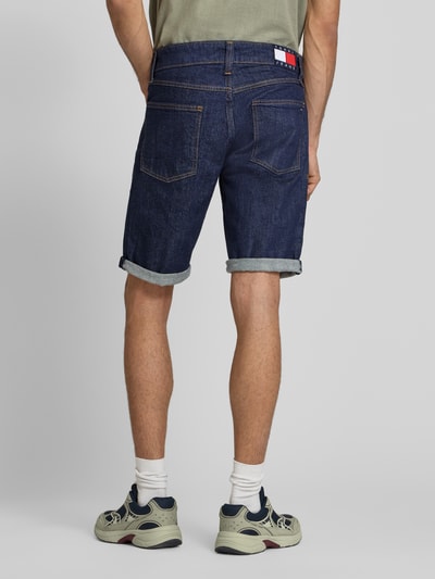 Männermodel trägt Regular Fit Jeansshorts aus Baumwoll-Mix von Tommy Jeans in dunkler Denim-Optik mit Label-Patch und 5-Pocket-Design, Ganzkörperansicht Rückansicht.