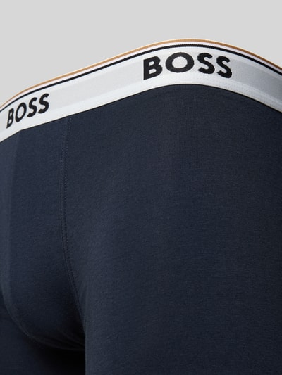 Mężczyznamodel nosi Trunks aus Baumwoll-Mix im 3er-Pack od BOSS, kolor granatowy, elastyczny biały pas z logo; zbliżenie tylnej części.