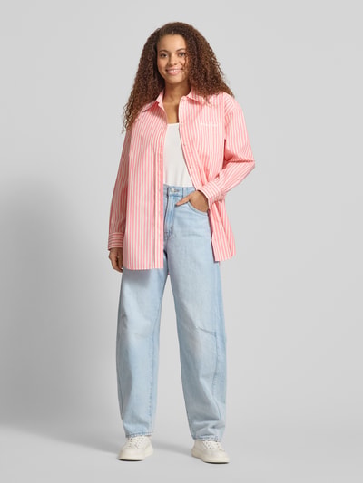 Frauenmodel trägt Oversized Hemdbluse aus Baumwoll-Mix von Tommy Jeans in Optik: Unifarben, Passform: Oversized, hellrosa mit weißen Streifen, Hemdkragen, Label-Schriftzug, Rückenpasse, einreihige Knopfleiste, langarm mit Manschette, leicht abgerundeter Rumpfabschluss, Materialverarbeitung: Popeline, Ganzkörperansicht von vorne.