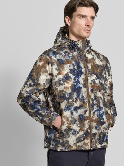 Mannelijk model draagt Blouson mit Kapuze und Zweiwege-Reißverschluss van ARMANI EXCHANGE in regular fit met allover-look in bruin, blauw en beige tinten, met capuchon met trekkoord, tweewegrits, ritszakken; ruglengte 71 cm, schouderbreedte 53 cm, borstwijdte 64 cm, mouwlengte 64 cm; close-up bovenlichaam vooraanzicht.