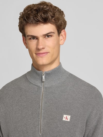 Männermodel trägt Loose Fit Troyer mit gerippten Abschlüssen von Calvin Klein Jeans in Grau mit kurzem Reißverschluss, Nahaufnahme Oberkörper.