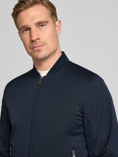 Männermodel trägt Bomberjacke mit Reißverschlusstaschen von Geox in Dunkelblau, glatte Struktur, Regular-Fit, Stehkragen, Nahaufnahme Oberkörper. Rückenlänge bei Größe M: 68 cm, Schulterbreite: 46 cm, Brustweite: 45 cm, Ärmellänge: 64 cm.