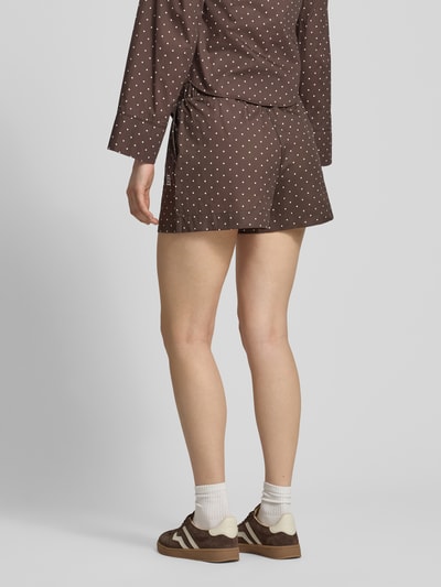 Modelka nosi brązowe Shorts mit elastischem Bund und Label-Detail Modell 'FRIDA' od Noisy May, wzór w białe kropki, materiał z bawełną, krój regular fit, szerokość w rozmiarze S 37 cm, długość nogawki wewnętrznej 9 cm, widok całej sylwetki z tyłu.