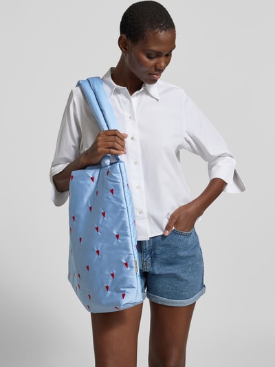 Frauenmodel trägt Tote Bag mit Allover-Motiv-Stitching Modell 'Puffy' von STUDIO NOOS, hellblau mit roten Akzenten, Ganzkörperansicht von vorne.