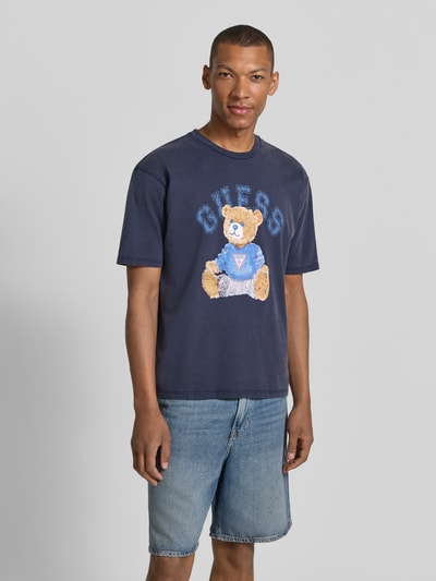 Männermodel trägt T-Shirt mit Motiv-Print und Rundhalsausschnitt von Guess, Herren T-Shirt aus Reine Baumwolle, Regular-Fit, Rückenlänge 68 cm, Vorderansicht Ganzkörperansicht.