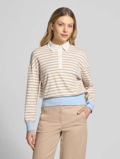 Frauenmodel trägt Regular Fit Poloshirt mit breitem Bund von Marc Cain in Beige, Weiß und Hellblau, Streifenmuster, Nahaufnahme Oberkörper. Elastischer Baumwoll-Mix, langärmlig mit Polokragen, überschnittene Schultern, elastische Abschlüsse, Rückenlänge 55 cm bei Größe 36.