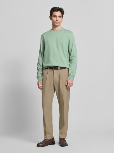 Männermodel trägt Regular Fit Gebreide pullover uit puur katoen Model 'UPCAS' van BOSS in effen lichtgroen, applicatie met labelstitching, ronde hals, lange mouwen, geribde mouwboord en rompzoom, materiaalverwerking knitwear. Ganzkörperansicht van voren.