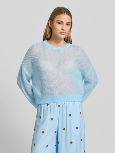Frauenmodel trägt sommerlicher cropped Strickpullover - curated by Mary Braun von Style Icon Collection in Hellblau, Strick-Optik, Relaxed-Fit, Rundhalsausschnitt, elastische Abschlüsse:, Rückenlänge bei Größe S 53 cm, Ärmellänge 72 cm, transparente Textur, Ganzkörperansicht von vorne.