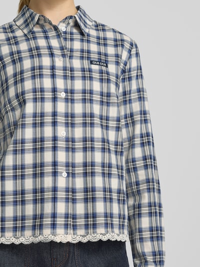 Frauenmodel trägt Regular Fit Hemdbluse aus reiner Baumwolle mit Spitzenbesatz von Oui, kariert in Blau-Weiß, Logo-Patch, Nahaufnahme Oberkörper. Hemdblusendesign, durchgehende Knopfleiste, Langarm, Spitzenbesatz am Saum, Kontext: Rückenlänge 57 cm, Ärmellänge 61 cm.