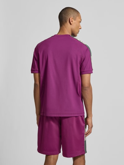 Mężczyzna model nosi T-shirt aus Viskose-Mix mit Logo od EA7 Emporio Armani, mieszanka wiskozy z dodatkiem streczu, krój regular fit, logo, okrągły dekolt, długość tyłu w rozmiarze M: 70 cm, fioletowe odcienie, gładka tekstura, widok całej sylwetki od tyłu.