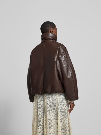 Frauenmodel trägt Oversized Jacke mit Leder-Anteil von Anine Bing, Material-Mix, gefütterter Stehkragen, Abdeckleiste, oversize, Rückenlänge 61 cm, Brustweite 64 cm, Ärmellänge 56 cm, Farbe Braun, glatte Struktur, Kontrast mit hellem Spitzenrock, Ganzkörperansicht Rückansicht.