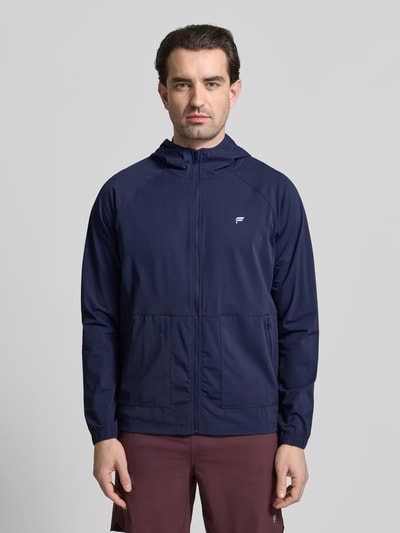 Männermodel trägt Regular Fit Jacke mit Logo-Print von Fabletics in Dunkelblau, Kapuze, Reißverschluss, glatte Textur, Ganzkörperansicht von vorne.