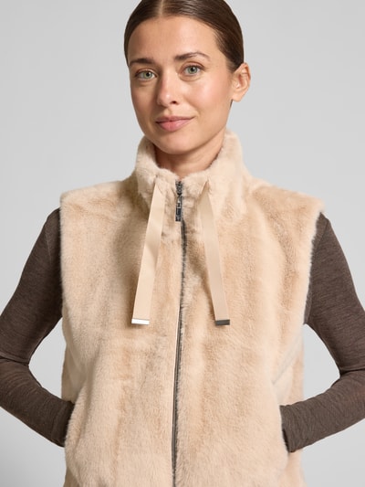 Vrouwenmodel draagt Weste aus Kunstfell mit Stehkragen und Reißverschluss van monari in beige, regular fit, tunnelkoord, rits, kunstbont, Nahaufnahme bovenlichaam.