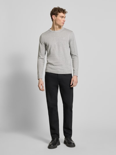 Męski model nosi Regular Fit Strickpullover aus reiner Baumwolle od Tom Tailor, szary, długi rękaw, krój regular fit, bawełna, gładka faktura, okrągły dekolt, naszyte logo, ściągacze, widok całej sylwetki z przodu.