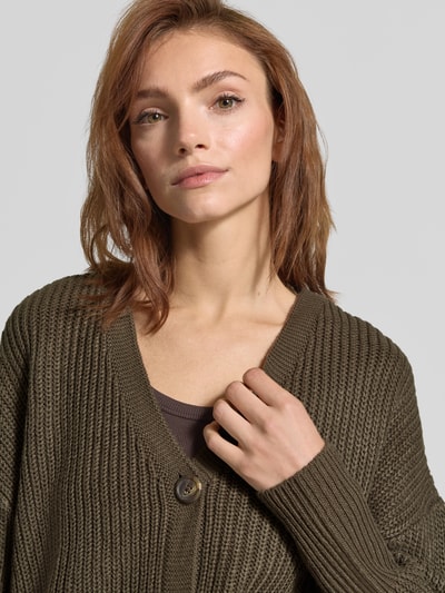 Frauenmodel trägt Oversized Strickjacke mit V-Ausschnitt Modell 'LEA' von VERO MODA, olivgrün, grob gestrickt, Nahaufnahme Oberkörper. Damen Strickjacke.