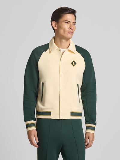Männermodel trägt Regular Fit Sweatjacke aus Baumwoll-Mix von Lacoste in Beige und Dunkelgrün mit gestreiften Bündchen, Ganzkörperansicht von vorne. Herren Sweatjacke von Lacoste.